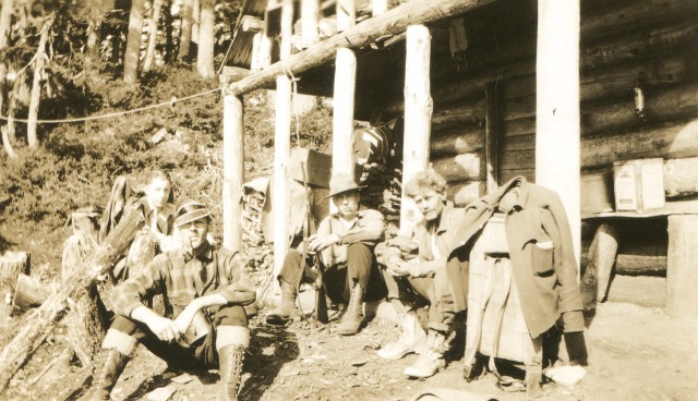 Sepia photo of men on the porch of a forest cabin.